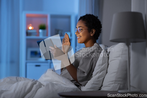 Image of woman with tablet pc in bed has video call at night