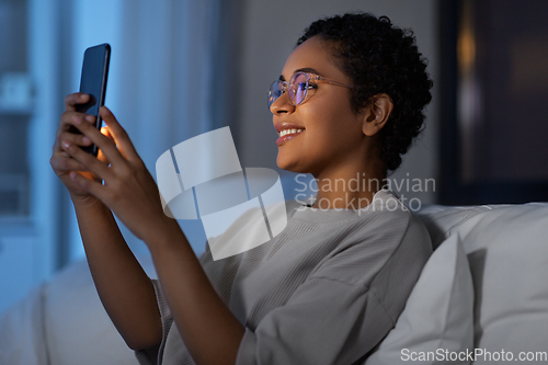 Image of african woman with smartphone in bed at night