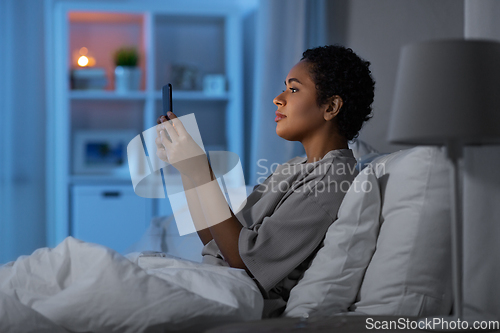 Image of african woman with smartphone in bed at night