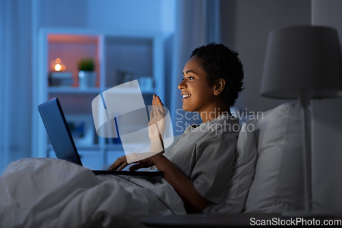 Image of woman having video call on laptop in bed at night