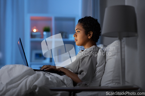 Image of woman with laptop in bed at home at night