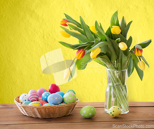 Image of colored easter eggs in basket and flowers on table