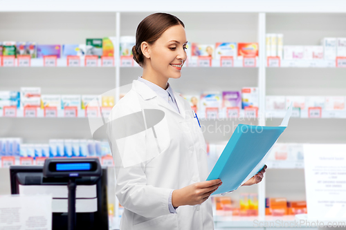 Image of smiling female doctor with folder at pharmacy