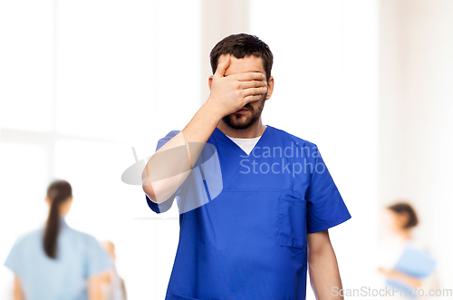 Image of tired doctor or male nurse covering eyes with hand