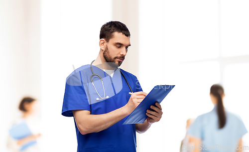 Image of male doctor writing medical report on clipboard