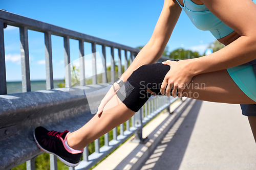 Image of young woman in knee band doing sports outdoors