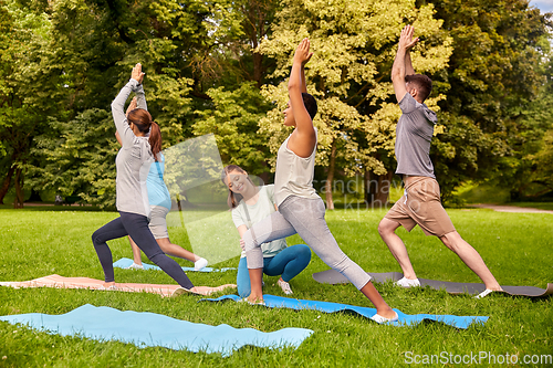 Image of group of people doing yoga with instructor at park