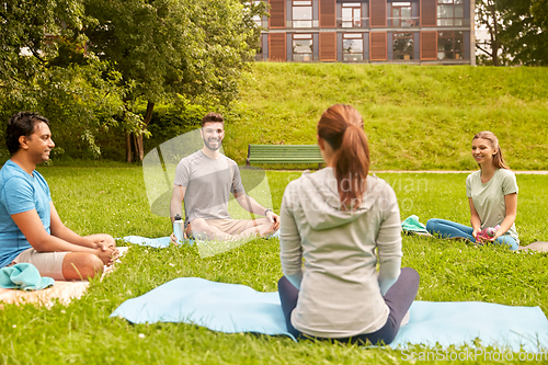 Image of group of people sitting on yoga mats at park