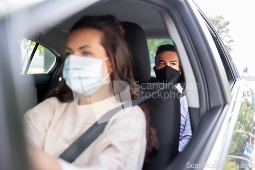 Image of female driver in mask driving car with passenger