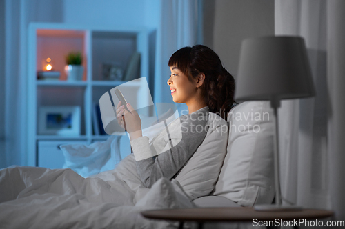 Image of asian woman with smartphone in bed at night