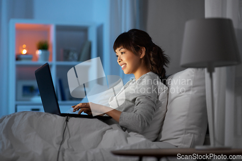 Image of woman with laptop in bed at home at night