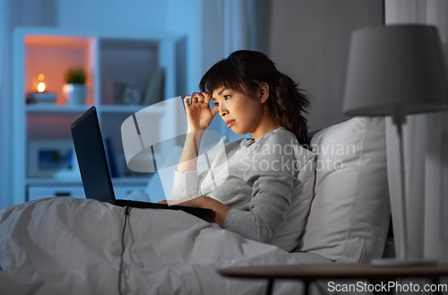 Image of stressed woman with laptop working in bed at night