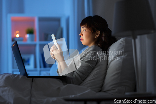 Image of asian woman with smartphone in bed at night