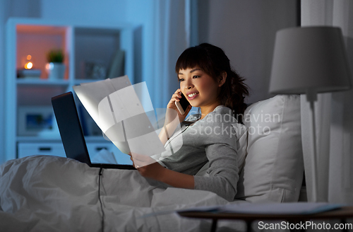 Image of woman with laptop calling on phone in bed at night