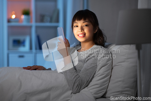 Image of asian woman with smartphone in bed at night