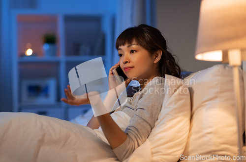 Image of asian woman calling on smartphone in bed at night