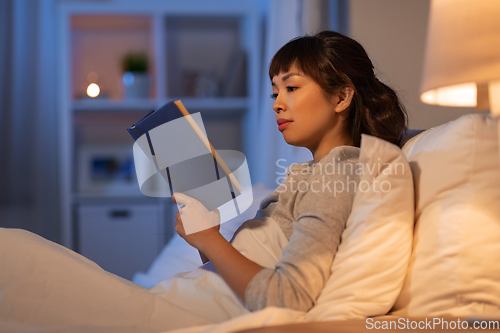 Image of young asian woman reading book in bed at home