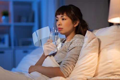 Image of asian woman drinking water at night in bed