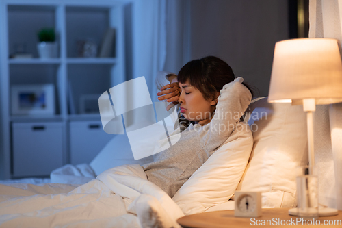 Image of tired asian woman stretching in bed at night