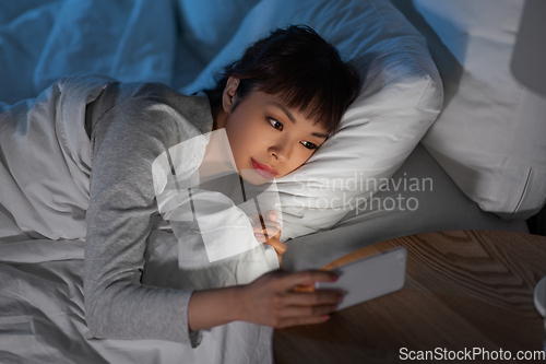 Image of asian woman with smartphone in bed at night