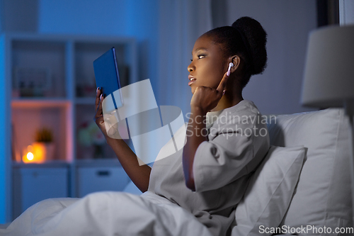 Image of woman with tablet pc and earphones in bed at night