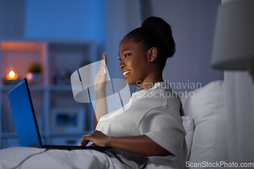 Image of woman with laptop has video call in bed at night
