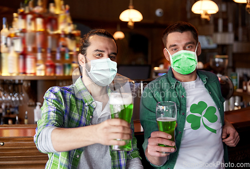 Image of male friends in masks drinking green beer at bar