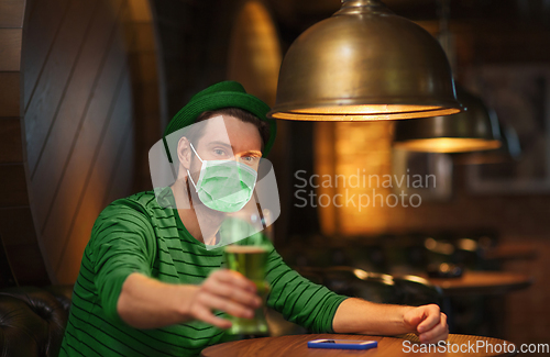 Image of young man in mask drinking green beer at bar