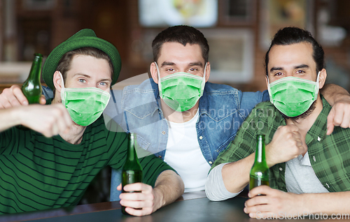 Image of male friends in masks drinking beer at bar or pub