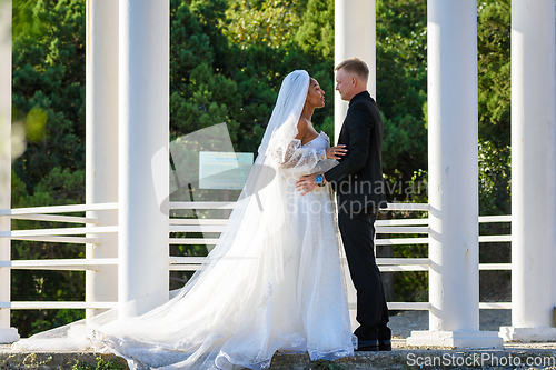 Image of Mixed-racial newlyweds on a walk hugging against the backdrop of a beautiful gazebo