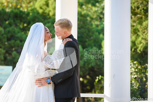 Image of Mixed-racial newlyweds on a walk hugging and lovingly look at each other