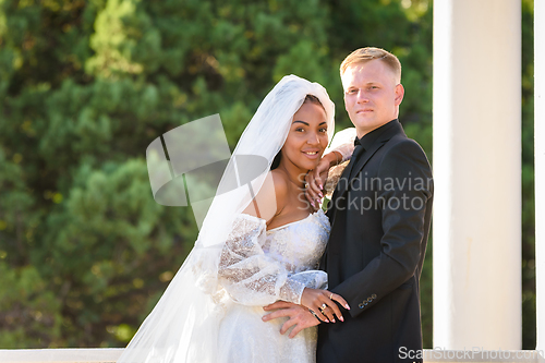 Image of Mixed race newlyweds on a walk hugging and looking into the frame