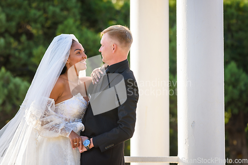 Image of Half-length portrait of mixed-racial newlyweds on a walk against the background of columns and greenery