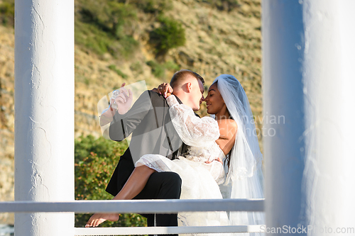 Image of Young beautiful interracial newlyweds kissing in the gazebo