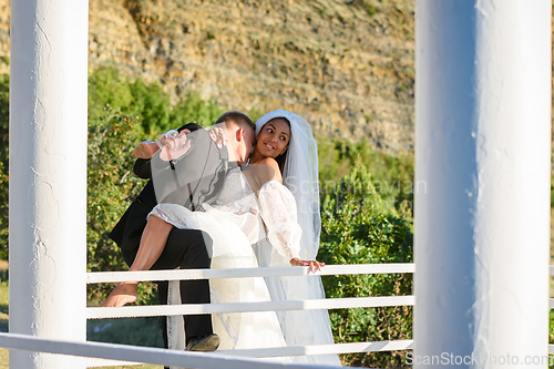 Image of Young beautiful interracial newlyweds hugging in the gazebo, the guy kisses the neck of the girl