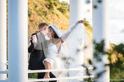 Image of Young beautiful interracial newlyweds hugging in the gazebo