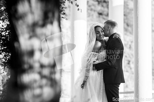 Image of Portrait of interracial newlyweds hugging against the background of columns, black and white photography