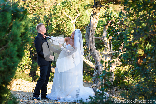 Image of Black bride strangles her white husband's tie against the backdrop of a sunny forest