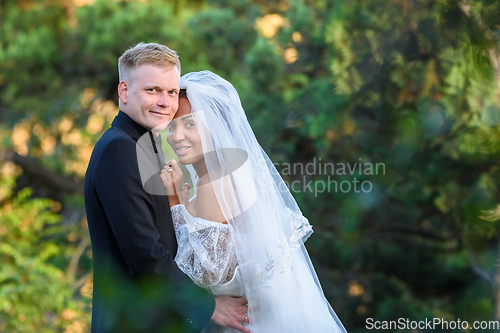 Image of Portrait of young beautiful interracial newlyweds on green foliage background