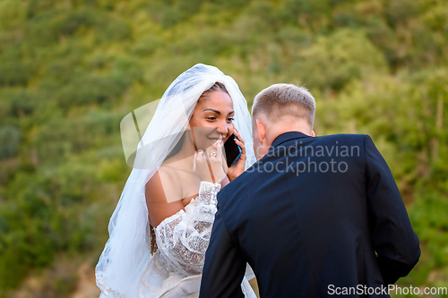 Image of A black bride accepts congratulations on the phone and looks happily at her white husband