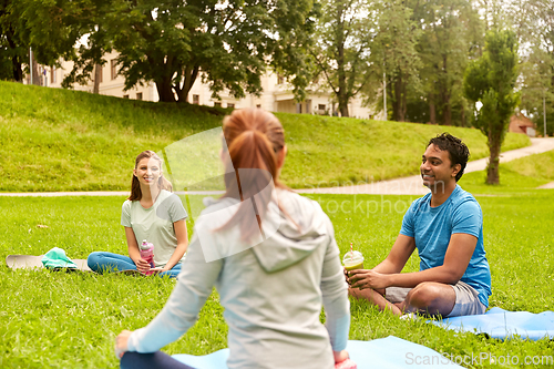 Image of group of people sitting on yoga mats at park