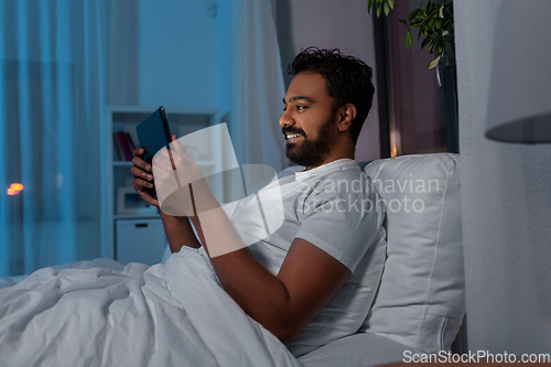 Image of indian man with tablet pc in bed at home at night