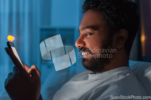 Image of indian man with smartphone in bed at home at night