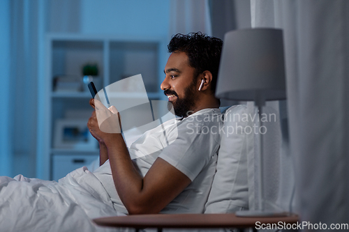 Image of man with smartphone and earphones in bed at night