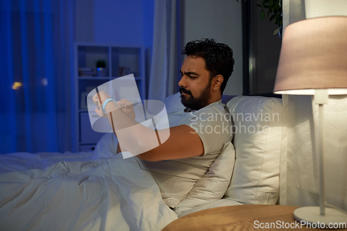 Image of indian man with health tracker in bed at night