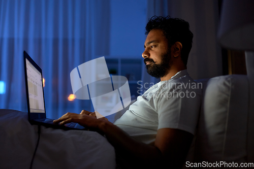 Image of indian man with laptop in bed at home at night