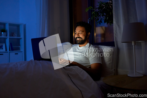 Image of indian man with laptop in bed at home at night