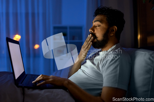 Image of indian man with laptop in bed at home at night