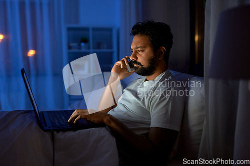 Image of indian man with laptop calling on phone at night