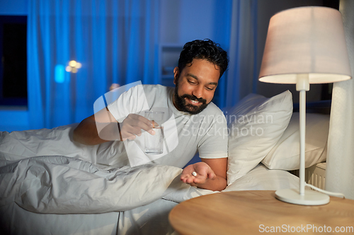 Image of indian man with medicine and water in bed at night